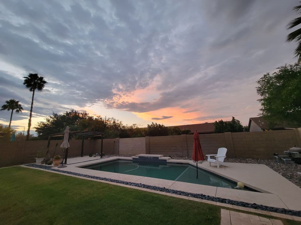 Serene backyard with pool, sunset sky, palm trees, and lounging chairs.