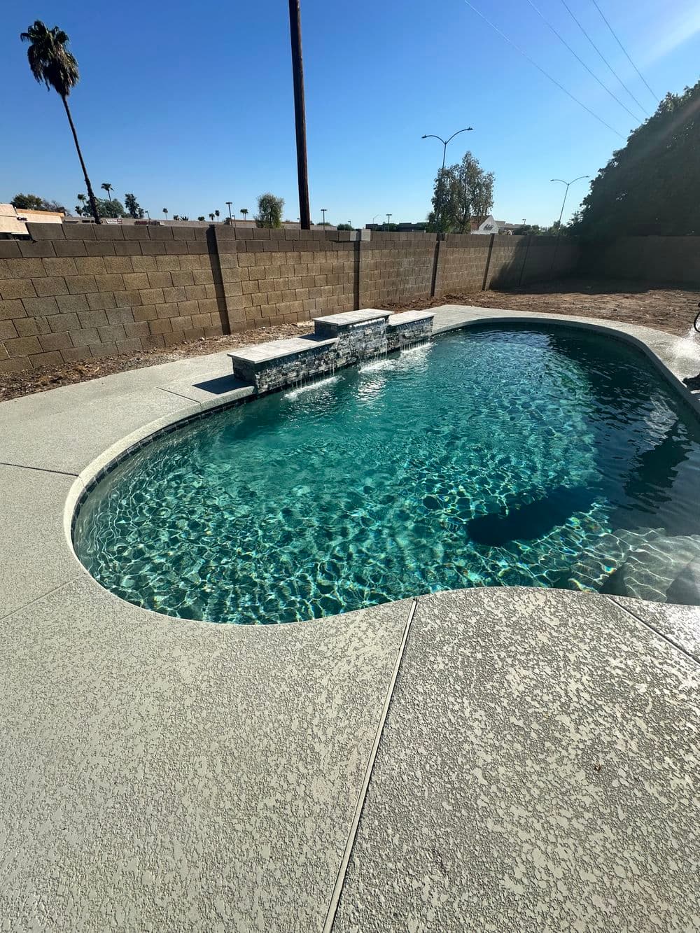 Sparkling blue pool with stone features in sunny backyard setting, surrounded by a fence.